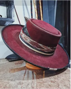 Detail of burgundy wool fedora featuring ethnic woven band and side feather decoration