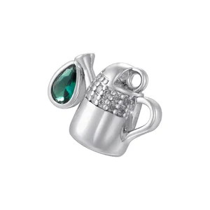 Macro shot of a silver watering can pendant with micro-pave crystals and a green gemstone