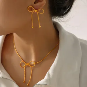 Detail of 18K gold-plated bow earrings and necklace set on a woman with white shirt