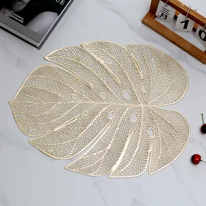 Golden monstera leaf PVC placemat with hollow design on white marble surface