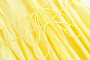 Makro-Detail des zitronengelben Kleides mit aufwendigen Schnürungen und Faltenstruktur