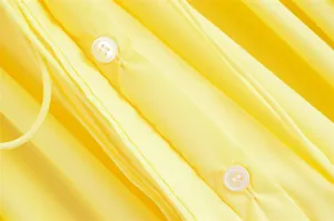 Detailansicht des zitronengelben Kleides mit Faltenstruktur und weißen Knöpfen
