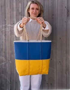 Detail of blue and yellow tote bag with rope handles held by a model outdoors