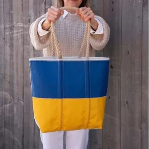 Large blue and yellow canvas tote bag with thick rope handles shown against a wooden fence