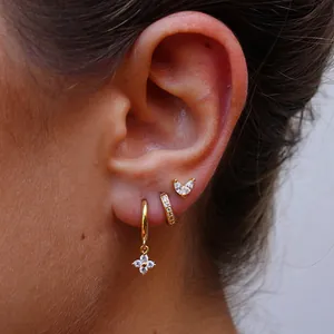 Vue détaillée de trois boucles d'oreilles trèfle dorées avec zircons portées par un mannequin
