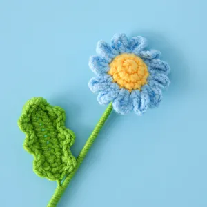 Gros plan d'une marguerite crochetée bleue avec cœur jaune et feuilles tricotées
