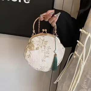 Close-up of white fabric bag with golden floral embroidery and green silk tassel detail