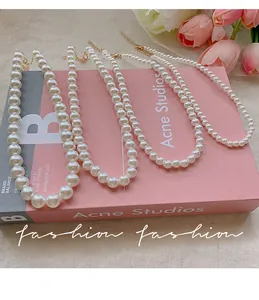 Close-up of four graduated pearl necklaces with golden lobster clasps on a pink book