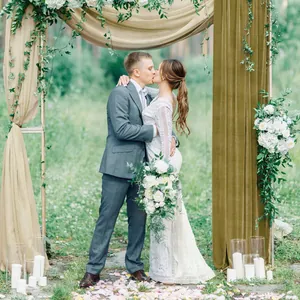 Close-up of champagne cheesecloth runner draped on wedding arch with floral decor