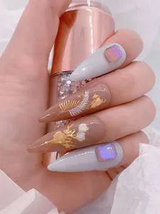 Detail of stiletto press-on nails with gold foil, white feathers, and purple rhinestones