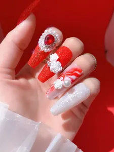 Detalle de uñas postizas largas con purpurina roja, relieve de rosa 3D y adornos de perla