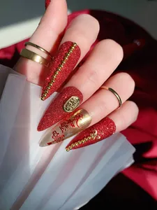 Vista detallada de uñas postizas rojas festivas con purpurina dorada y arte chino