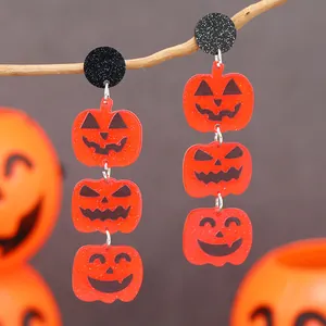 Three-tier orange acrylic Halloween pumpkin earrings on a rustic branch with glitter studs