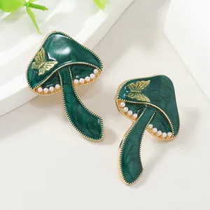 Detalle de aretes de hongo verde con mariposa dorada e incrustaciones de perlas blancas