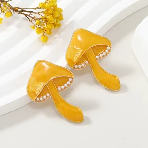 Detalle de pendientes de hongo amarillo con diseño de mariposa y micro perlas blancas
