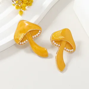 Detalle de pendientes de hongo amarillos con perlas y relieve de mariposa de moda