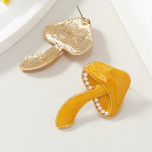 Detalle de pendientes de hongo amarillo con borde de perlas y relieve de mariposa