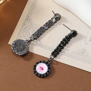 Close-up of black metal tassel earrings with pink devil eye pendant and crystals