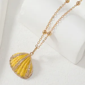Gros plan du pendentif coquillage jaune avec dorure et collier chaîne à perles