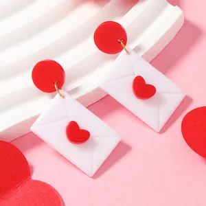 Vue détaillée des boucles d'oreilles enveloppe en acrylique avec coeur rouge et doré