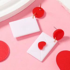 Détail de boucles d'oreilles enveloppe en acrylique avec cœur rouge sur fond rose
