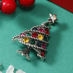 Dettaglio ravvicinato di una spilla a albero di Natale argento con strass colorati su sfondo verde