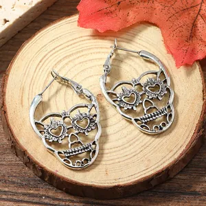 Gothic skull hoop earrings with heart-shaped eyes on natural wood background