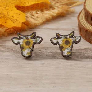 Cow head stud earrings with vibrant sunflower pattern on rustic wood texture