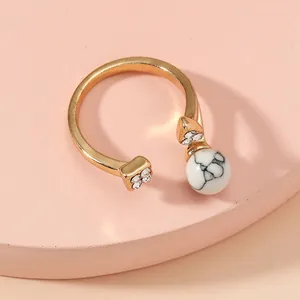 Close-up of adjustable gold ring with square diamonds, white marble bead, and heart detail