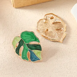 Vue détaillée de boucles d'oreilles monstera en métal doré avec émail vert dégradé