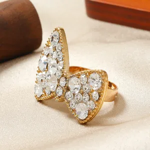 Dettaglio macro di un anello a farfalla dorato con cristalli scintillanti su raso beige