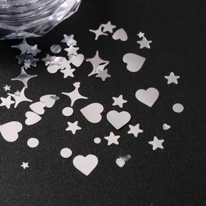 Macro view of silver mixed heart and star nail art sequins on a dark background