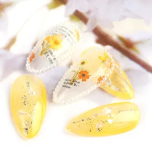 Close-up of almond nails with yellow flowers, micro pearls and French script details