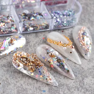 Macro detail of mixed nail art charms including metal butterflies, pearls and glitter flakes