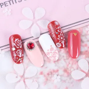 Dettaglio di unghie finte con pietre preziose rosse e motivi floreali bianchi eleganti