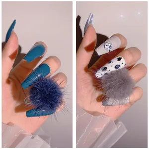Dettaglio di unghie finte lunghe con pompon di peluche blu scuro e motivi a mucca