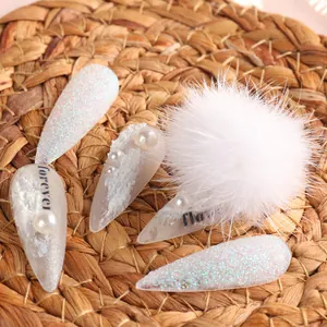 Dettaglio del pompon bianco rimovibile e accenti di perle su eleganti unghie finte