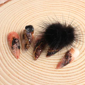 Dettaglio di unghie finte stiletto gotiche con gemma nera, catena e pompon di pelliccia