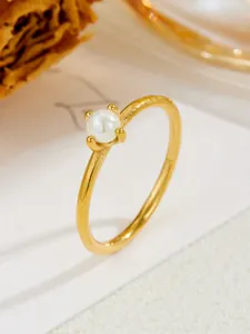 Close-up of a delicate pearl ring with a gold four-prong setting and fine titanium band