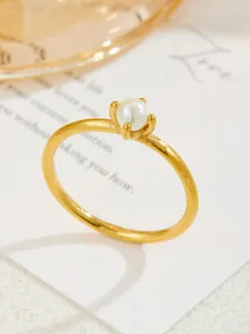 Detailed close-up of a single white pearl secured by a four-prong setting on a gold ring