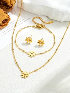 Detailed set of gold titanium daisy necklace, bracelet and earrings on a white stone background