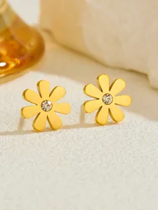 Macro shot of gold-plated daisy earrings with center zircon on a textured stone surface