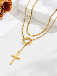 Detalle del collar en Y dorado con colgante de cruz y cadena de cuentas multicapa