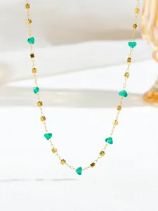 Detail van gouden ketting met groene hartkristallen en vierkante kralen op witte achtergrond