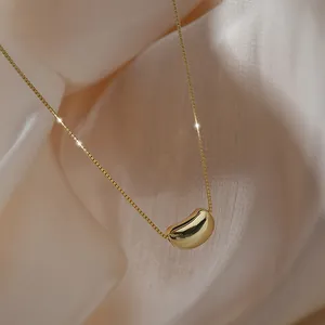 Elegante Halskette aus Gold Titanstahl mit poliertem Bohnenanhänger auf Seidenhintergrund