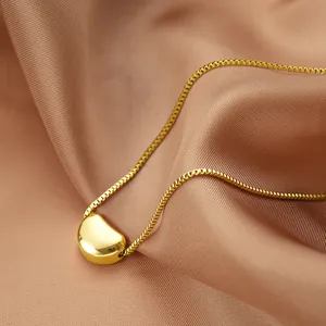 Minimalistische goldene Titanstahlkette mit poliertem Bohnenanhänger auf Seidenstoff