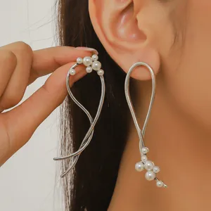Detalle de pendientes largos asimétricos en acabado plateado con perlas blancas finas