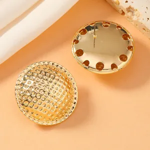 Macro shot of gold geometric earrings with textured checker pattern and hollow edges
