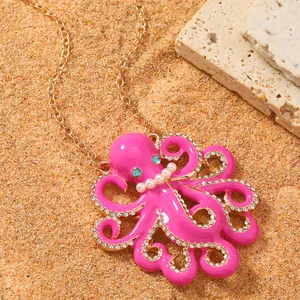 Detail van de roze geëmailleerde octopus hanger met blauwe strassteentjes op zand