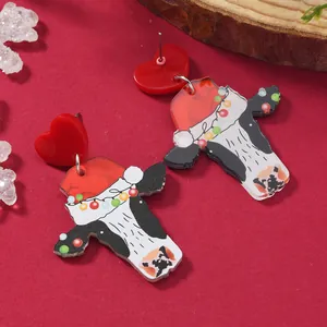 Close-up of cute cow acrylic earrings with Santa hat and festive lights on red background